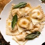 A cropped square image of butternut squash ravioli in a bowl with sage.