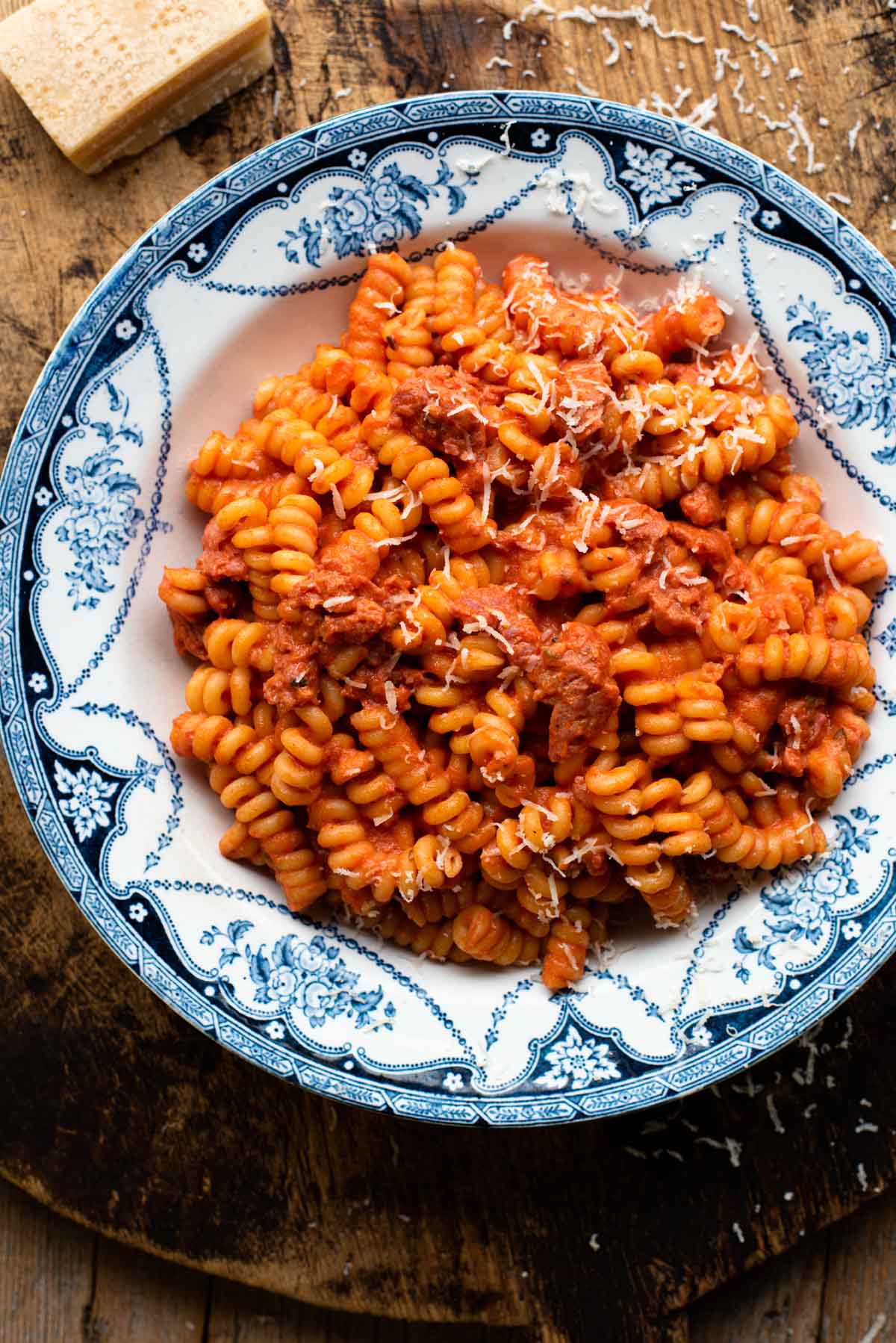Creamy tomato pasta with sausage in a blue patterned bowl on a wooden serving board. 