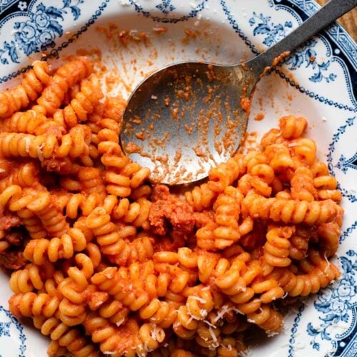 An overhead shot of creamy tomato pasta with Italian sausage in a blue patterned bowl with a serving spoon at the side.