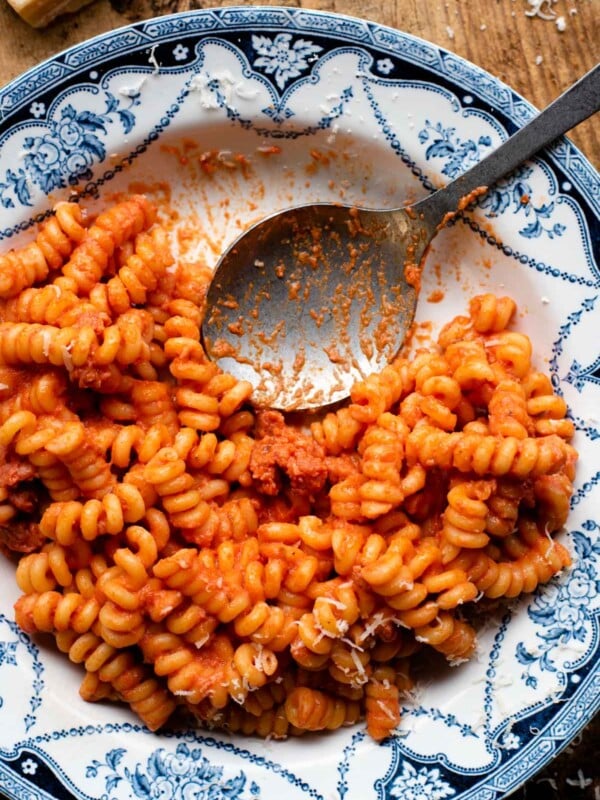 An overhead shot of creamy tomato pasta with Italian sausage in a blue patterned bowl with a serving spoon at the side.