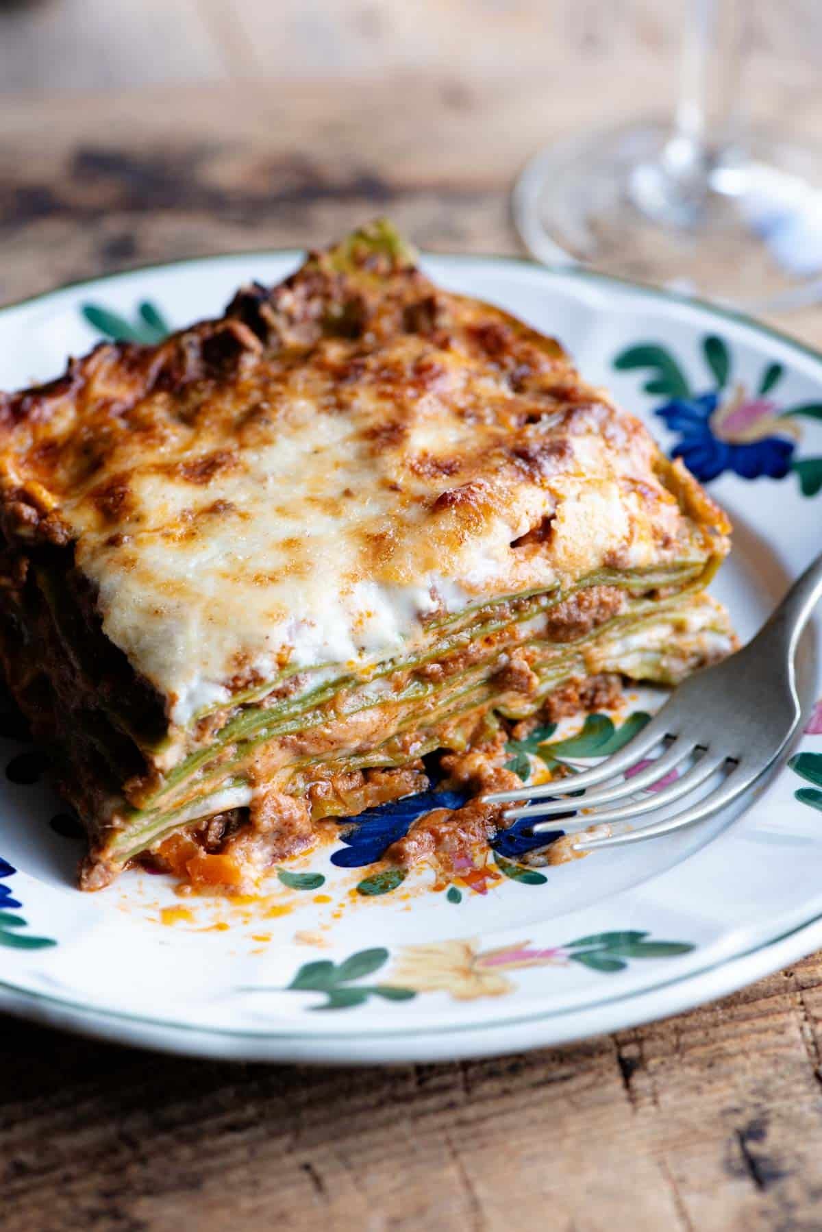 A close up of a slice of Lasagna Bolognese on a plate with a flower pattern.