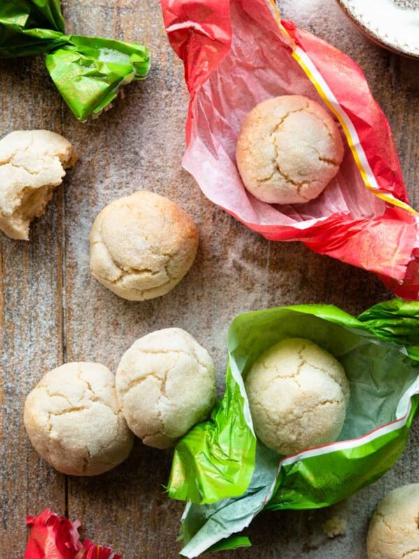 An overhead shot of amaretti cookies on a wooden surface some in pink and green wrappers.