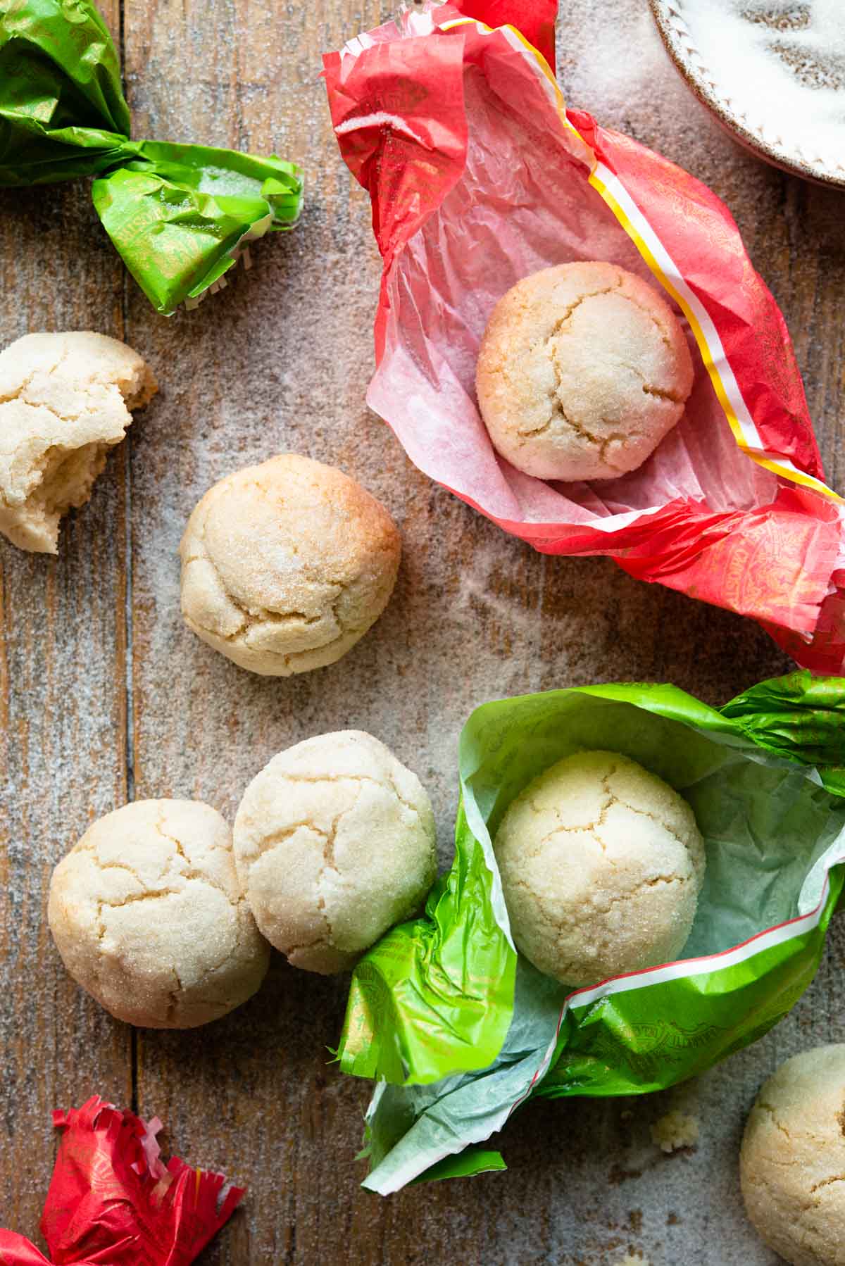 An overhead shot of amaretti cookies on a wooden surface some in pink and green wrappers.