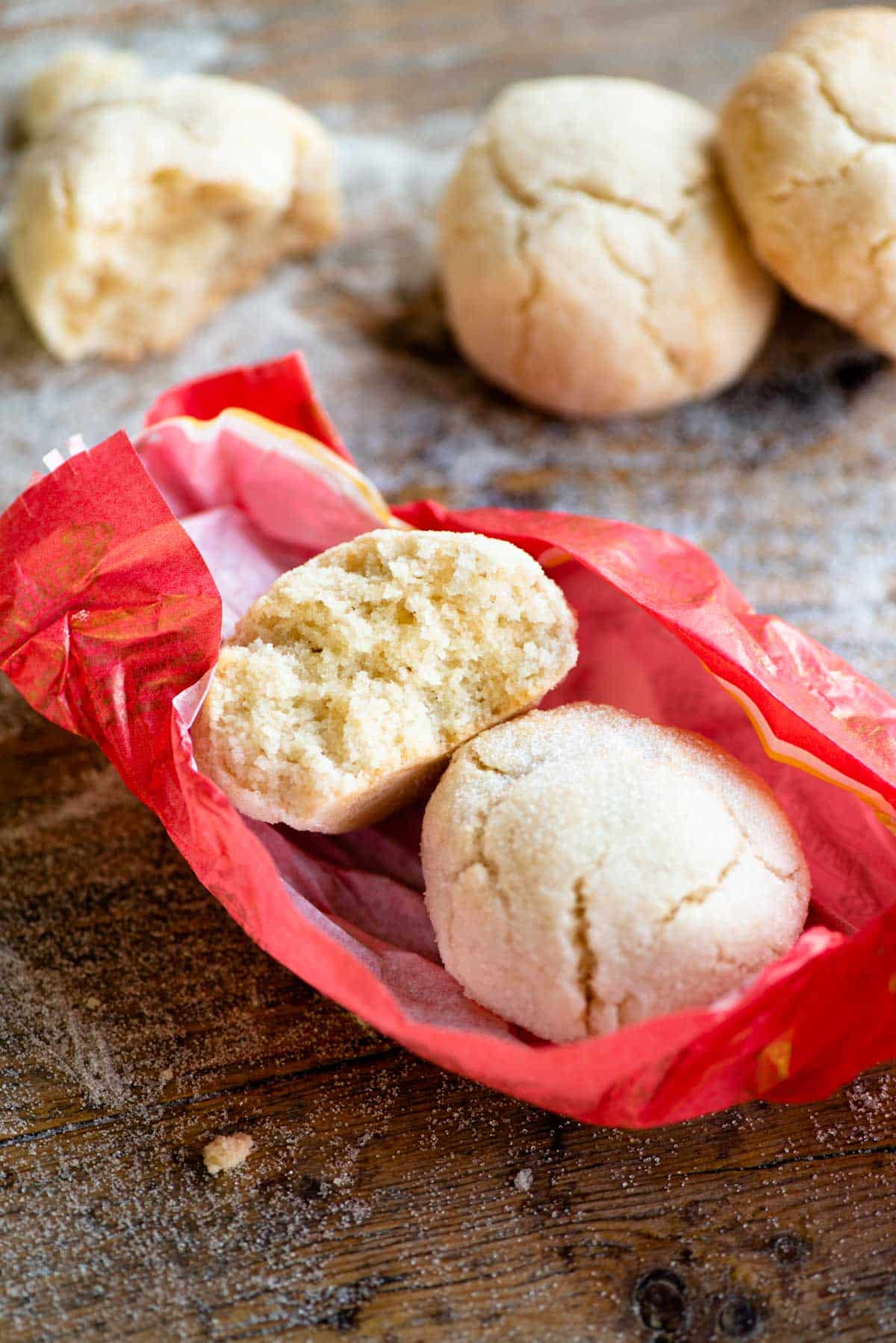 A close up of two amaretti cookies in a pink wrapper, one cut in half to see the texture inside.