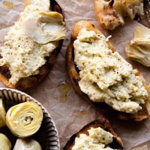 A cropped close up of 3 pieces of artichoke bruschetta sitting on baking parchment.