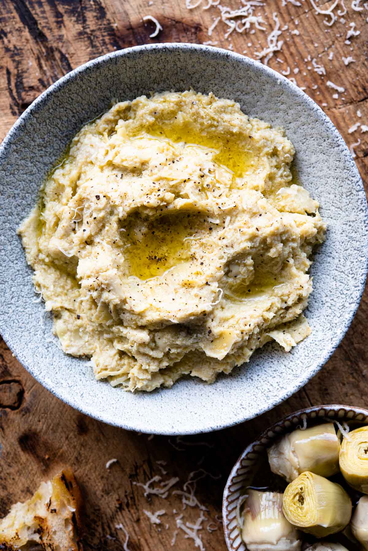 Artichoke pesto in a blue bowl sitting on a wooden surface.