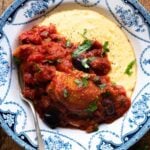 A cropped close up of chicken puttanesca with creamy polenta in a blue bowl.