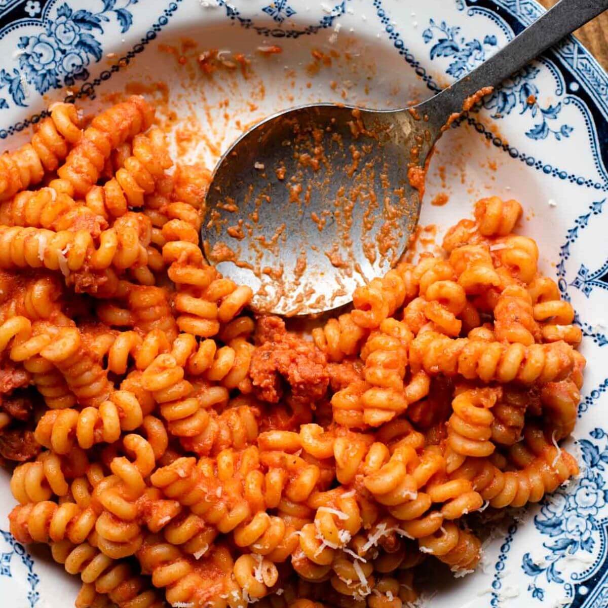 Creamy tomato sausage pasta in a blue patterned bowl with a serving spoon