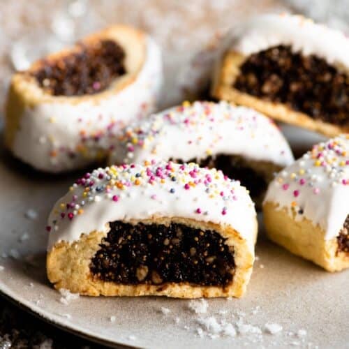 Five Cuccidati cookies on a plate with fake white snow scattered around.