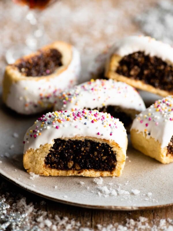 Five Cuccidati cookies on a plate with fake white snow scattered around.