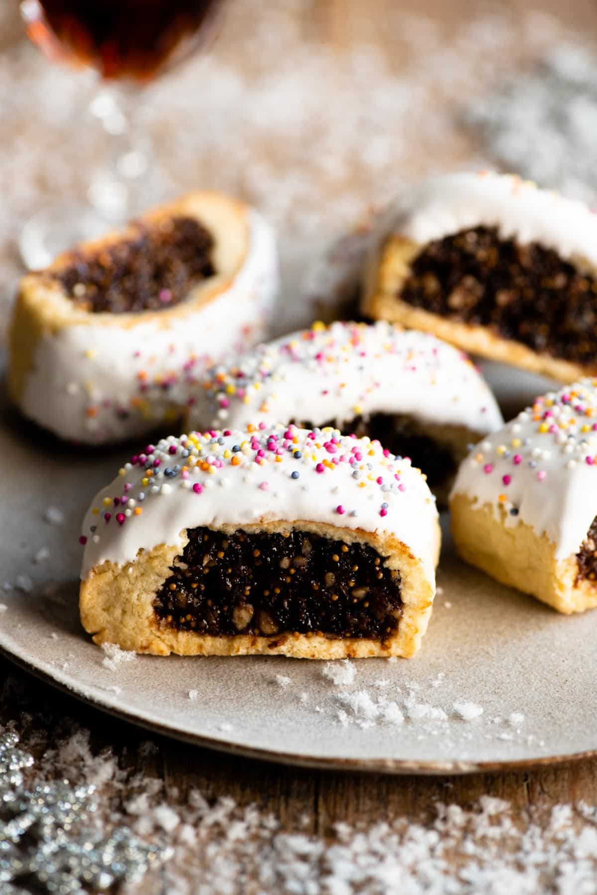 Five Cuccidati cookies on a plate with fake white snow scattered around.