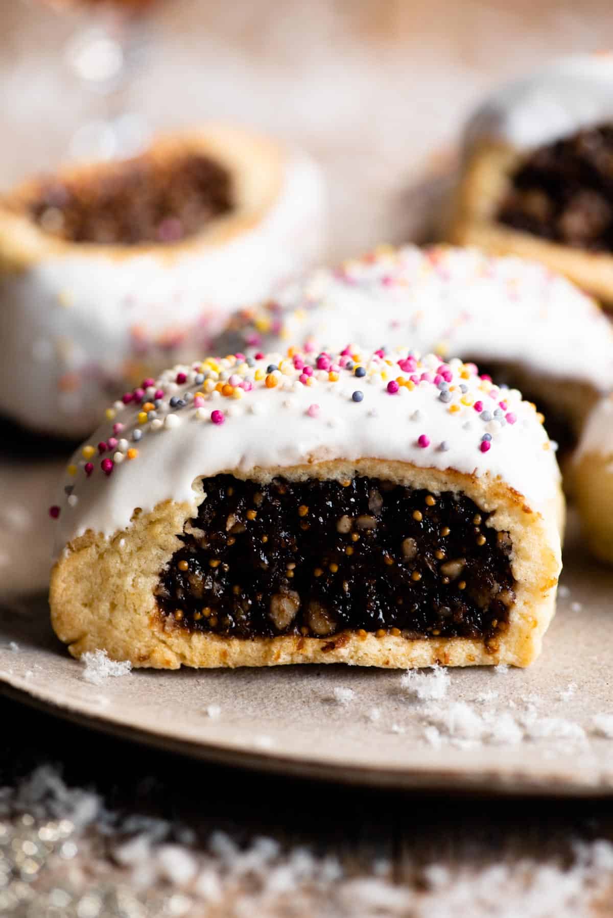 A close up of a cuccidati cookie topped with white icing and coloured sprinkles.