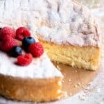 A square image of an Italian sponge cake (Pan di Spagna) close up with a slice cut out and berries on top.