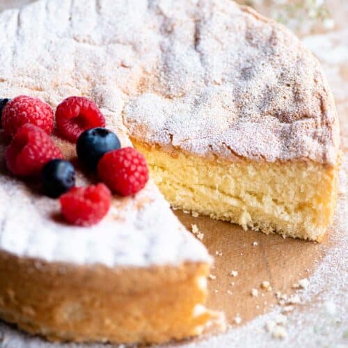 A close up of an Italian Pan di Spagna sponge cake with a slice cut out and berries on the top.