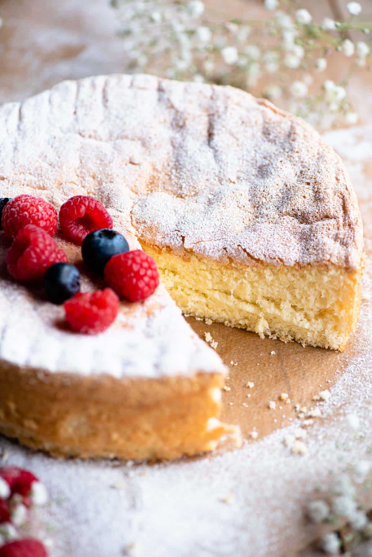 A close up of an Italian Pan di Spagna sponge cake with a slice cut out and berries on the top.