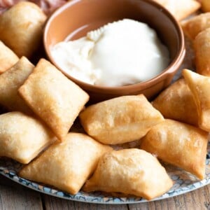 A close up square image of Gnocco Fritto (Italian fried dough) on a plate with cheese.