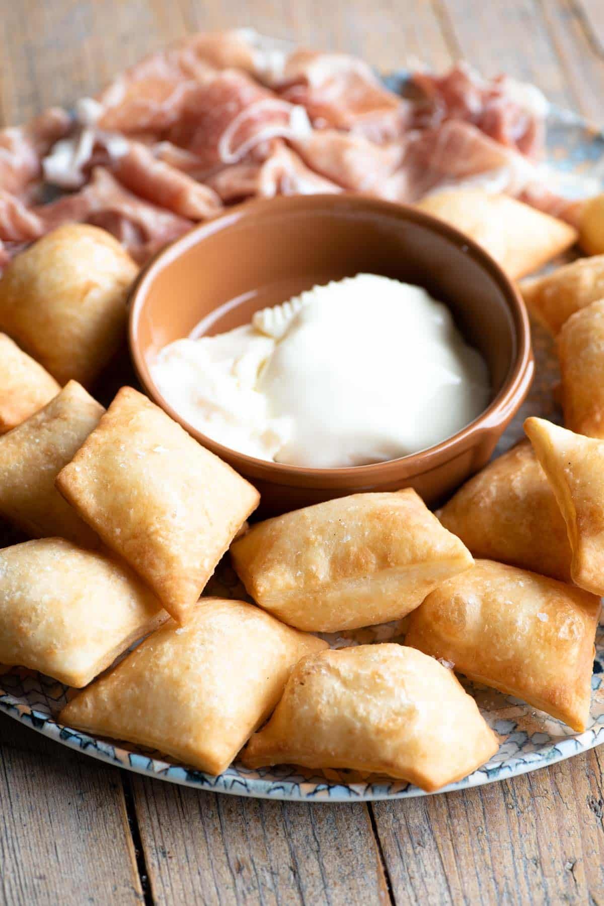 A close up of gnocco fritto (fried dough) on a plate with meat and cheese.