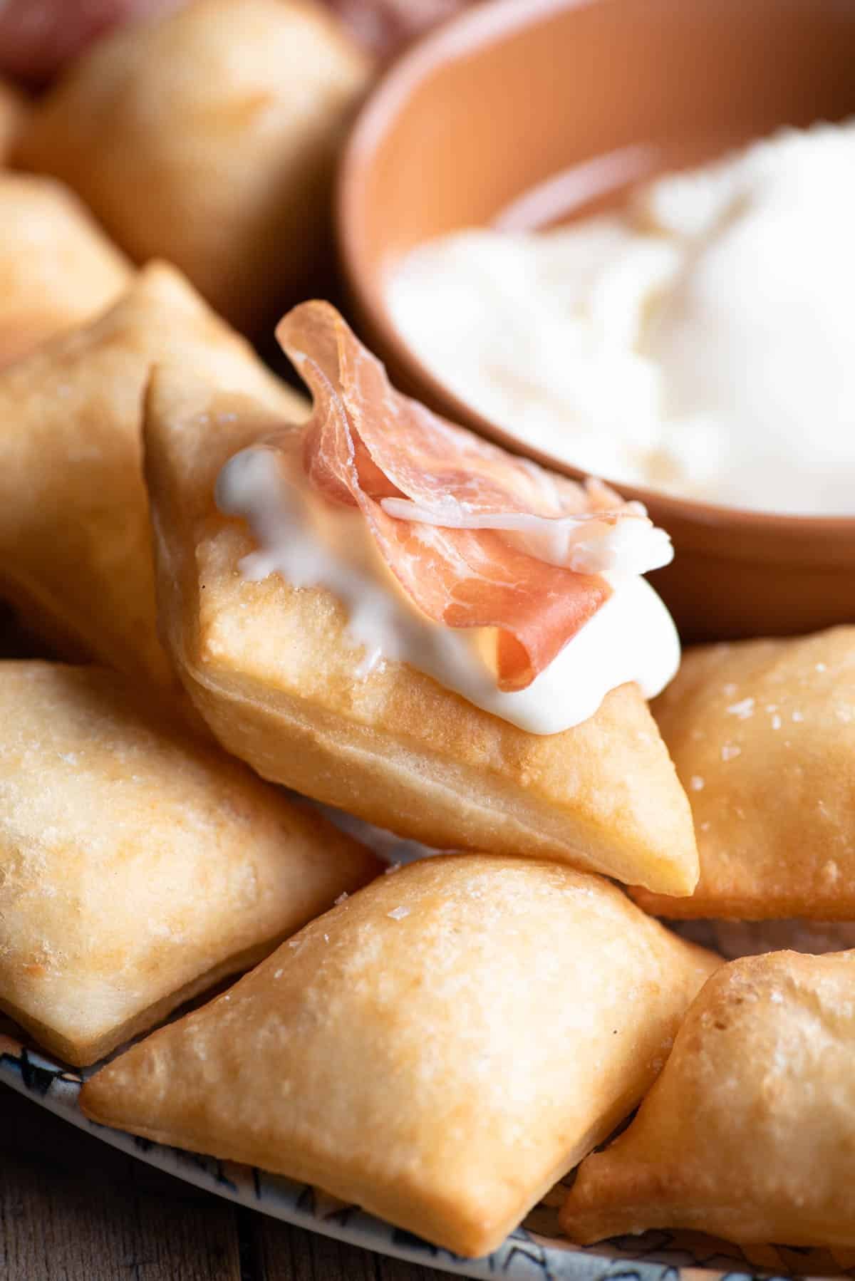 A close up of Gnocco Fritto (Italian fried dough) with cheese and prosciutto on top.