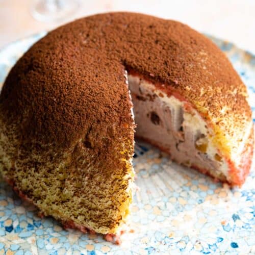 A dome shaped Italian dessert called Zuccotto on a patterned plate with a slice cut out.