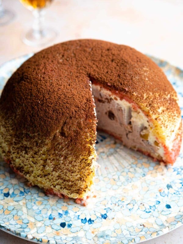 A dome shaped Italian dessert called Zuccotto on a patterned plate with a slice cut out.