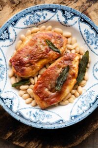 Two pieces of chicken saltimbocca on a plate on top of cannellini beans.