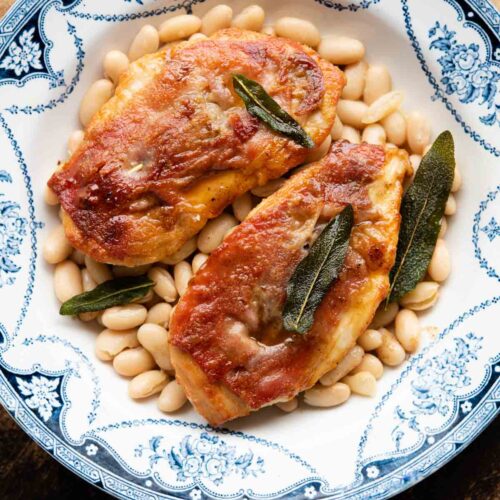 Two pieces of chicken saltimbocca on a plate on top of cannellini beans.