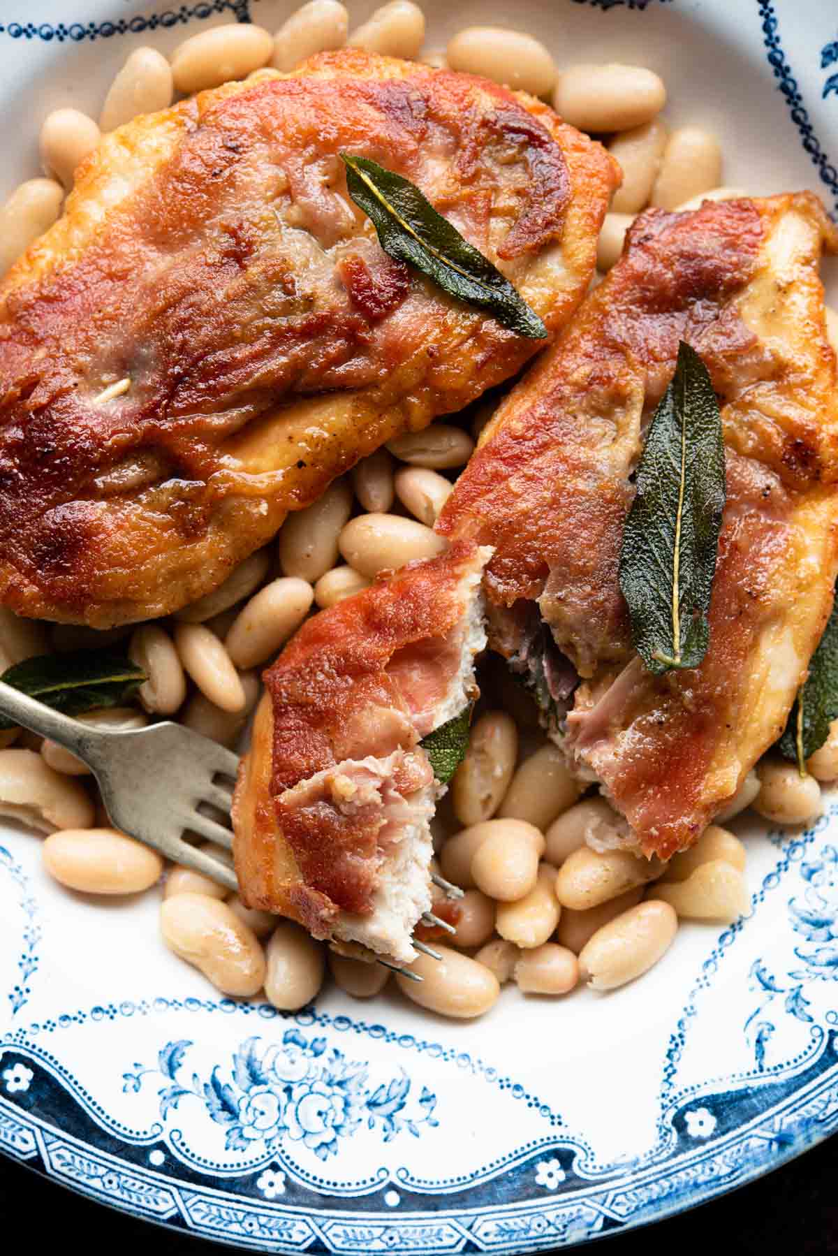 A close up of chicken saltimbocca on a plate with beans and sage.