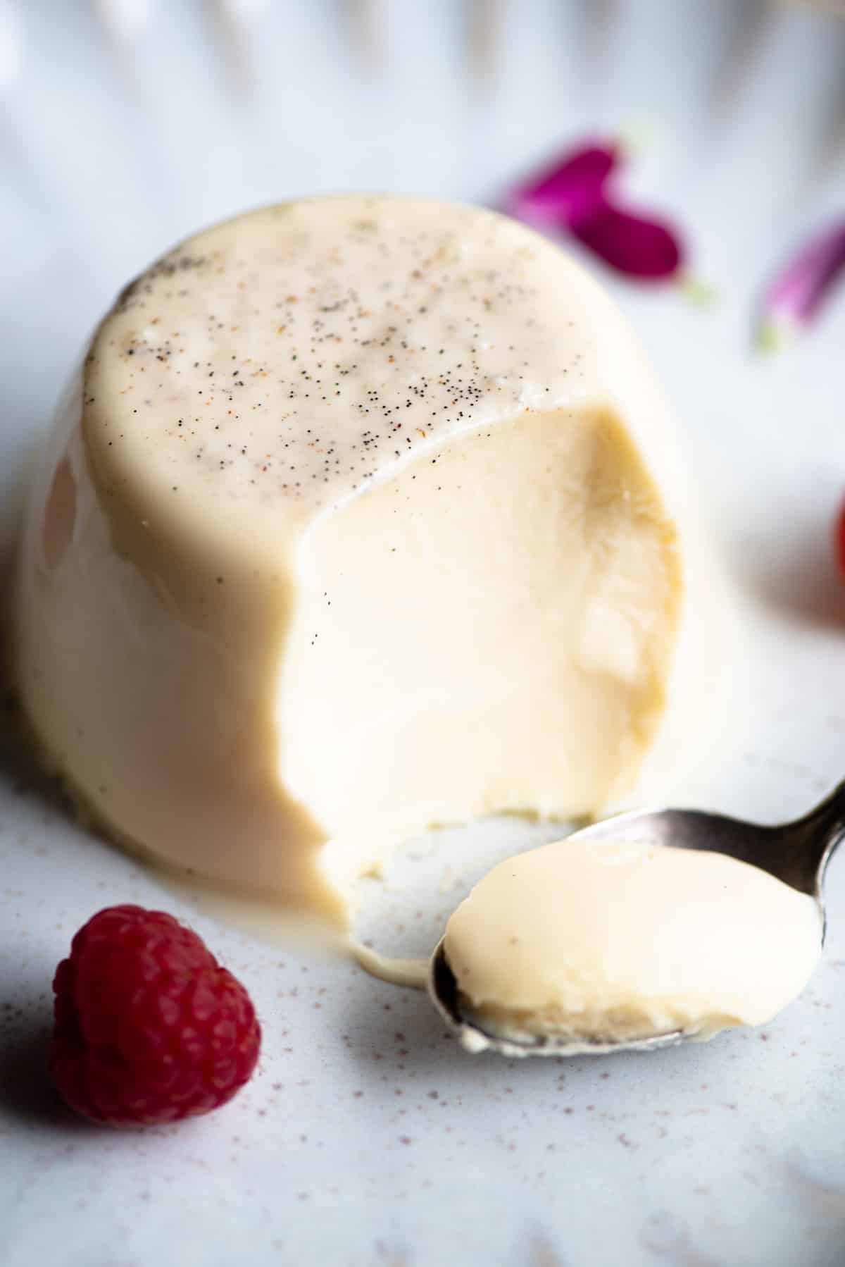 A close up of a vanilla panna cotta with a bite out and spoon at the side.
