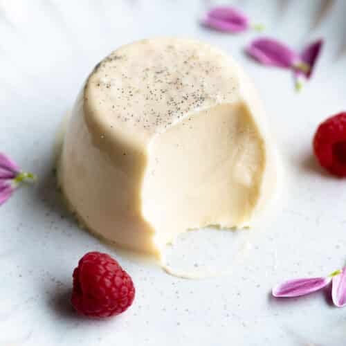 A vanilla panna cotta on a plate with a bite out and raspberries at the side.