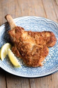 Veal Milanese (veal cutlet) on a blue plate with lemon wedges at the side.