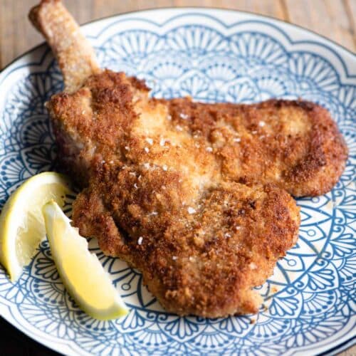 Veal Milanese (veal cutlet) on a blue plate with lemon wedges at the side.