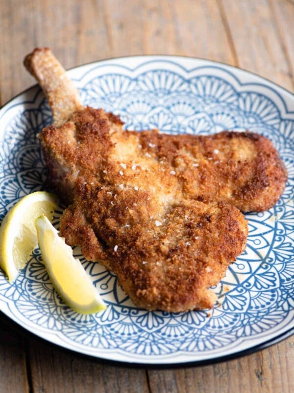 Veal Milanese (veal cutlet) on a blue plate with lemon wedges at the side.