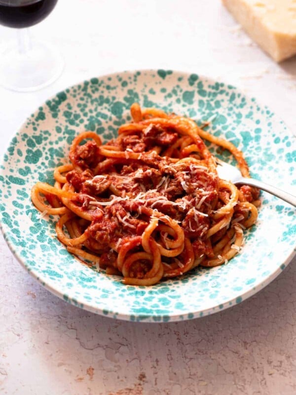 Tuscan sausage pasta with pici in a blue bowl on a light work surface.