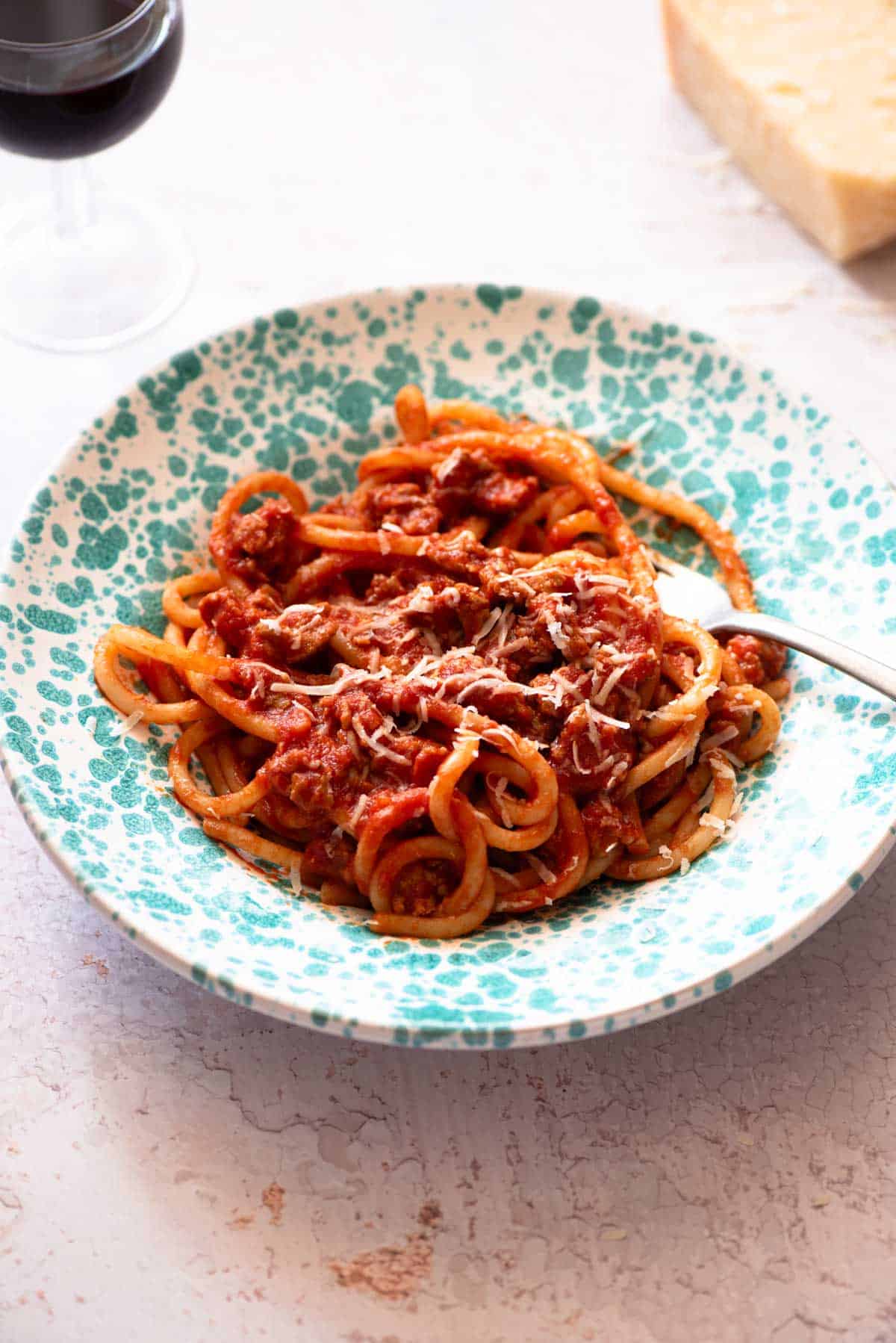 Tuscan sausage pasta with pici in a blue bowl on a light work surface.