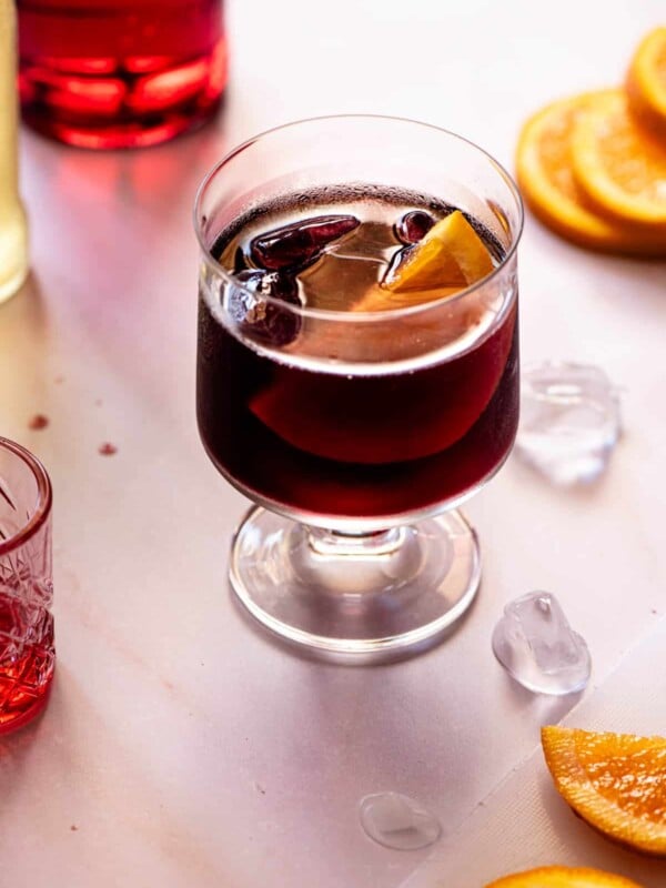 A red wine spritz (prampolini) on a light background with slices of orange, ice and campari at the side.