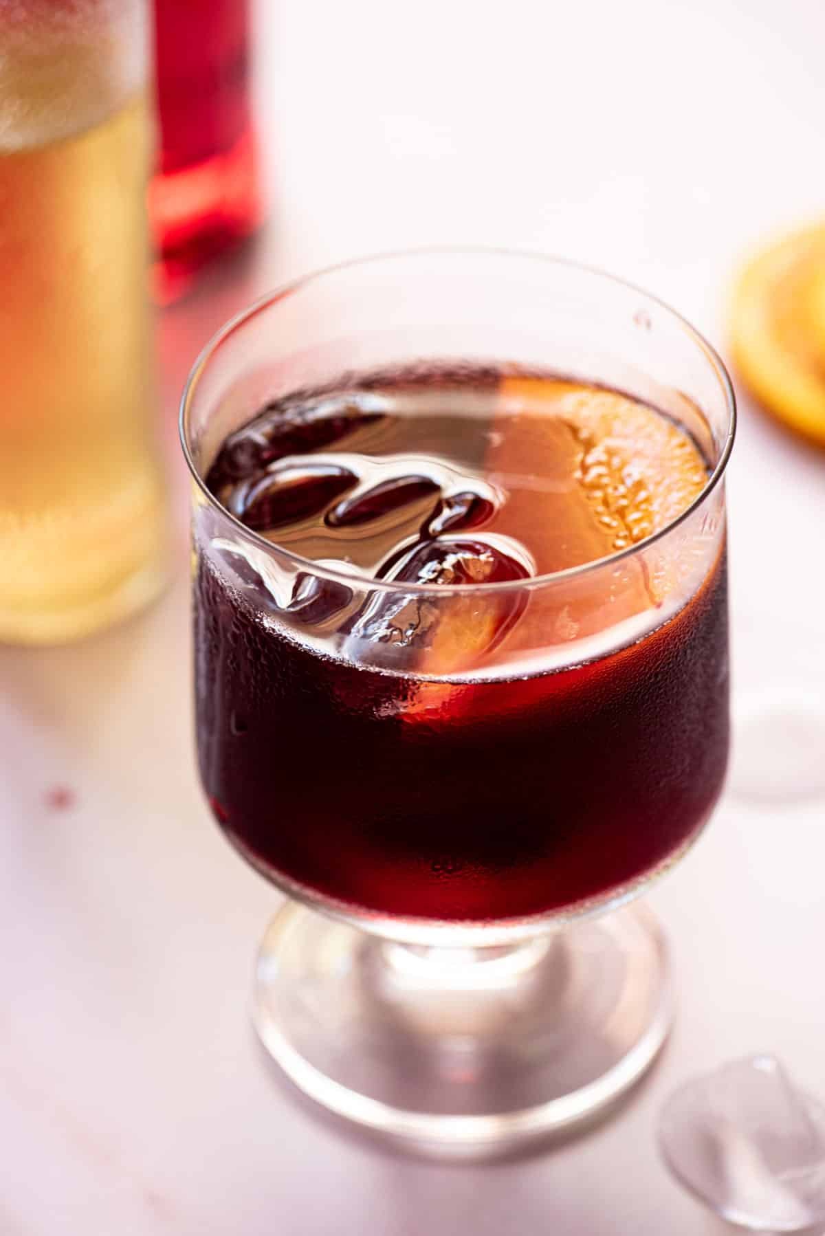 A close up of a red wine spritz in a glass with a slice of orange.