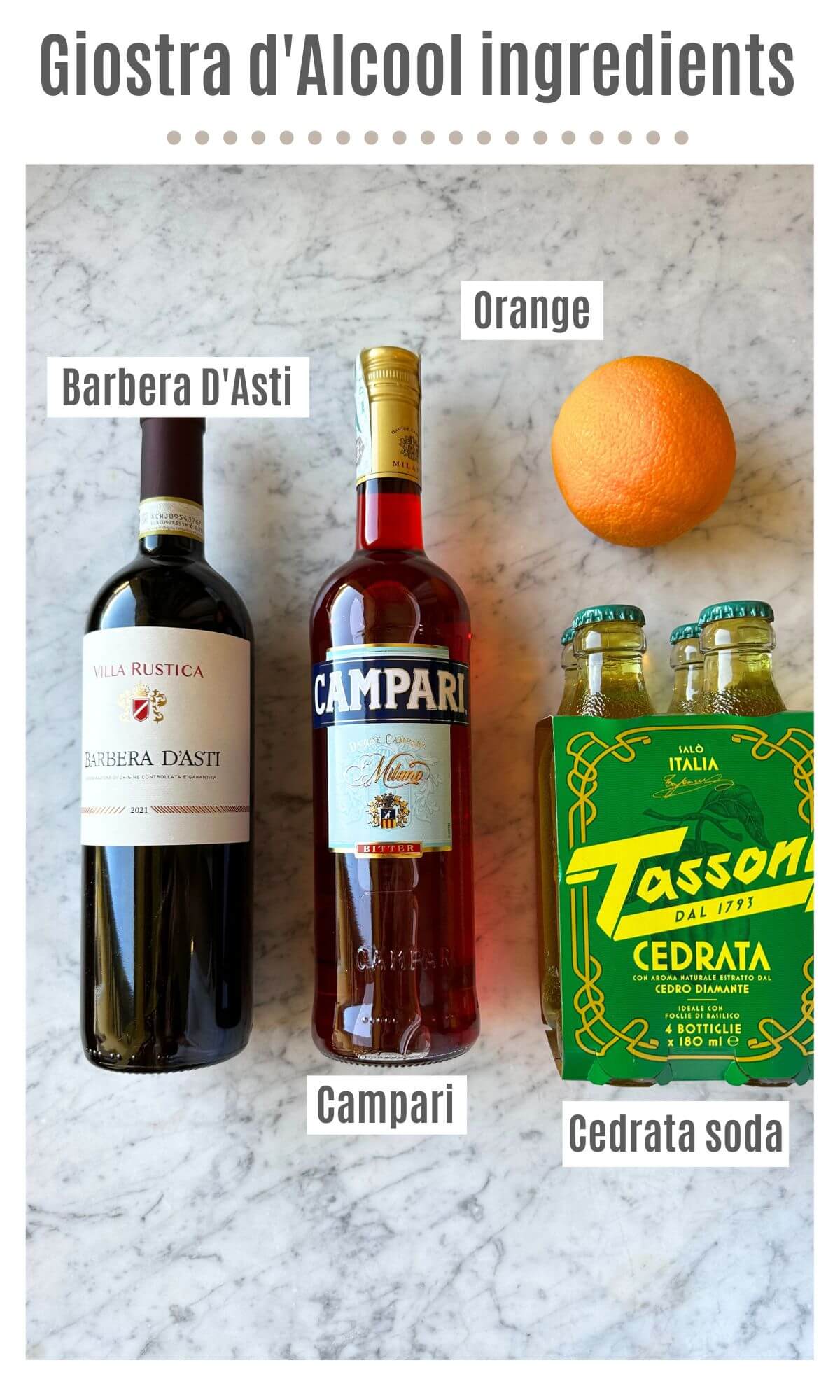 An overhead shot showing all the ingredients to make an Italian red wine spritz; Barbera D'Asti, Campari, Cedrata soda and an orange on a marble worktop.