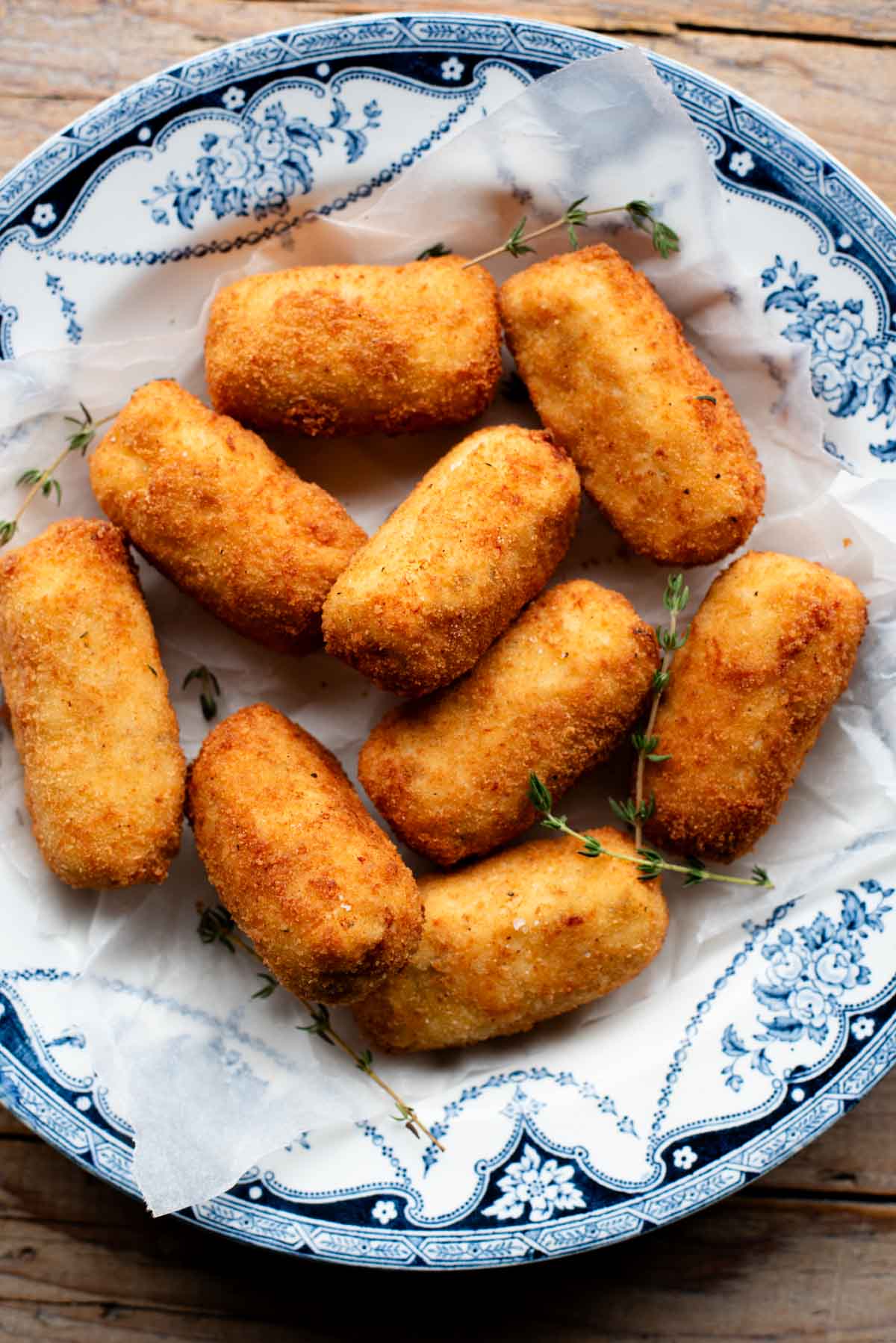 An overhead shot of chicken croquettes in a blue bowl with sprigs of thyme.