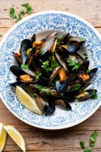 An overhead shot of peppered mussels in a blue bowl with fresh parsley and lemon.