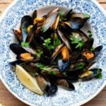 A cropped image of mussels in a blue bowl topped with fresh parsley and lemon.