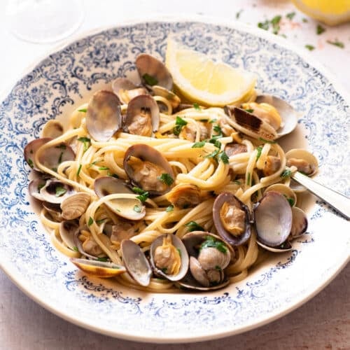Linguine alle Vongole in a blue bowl with a slice of lemon at the side.