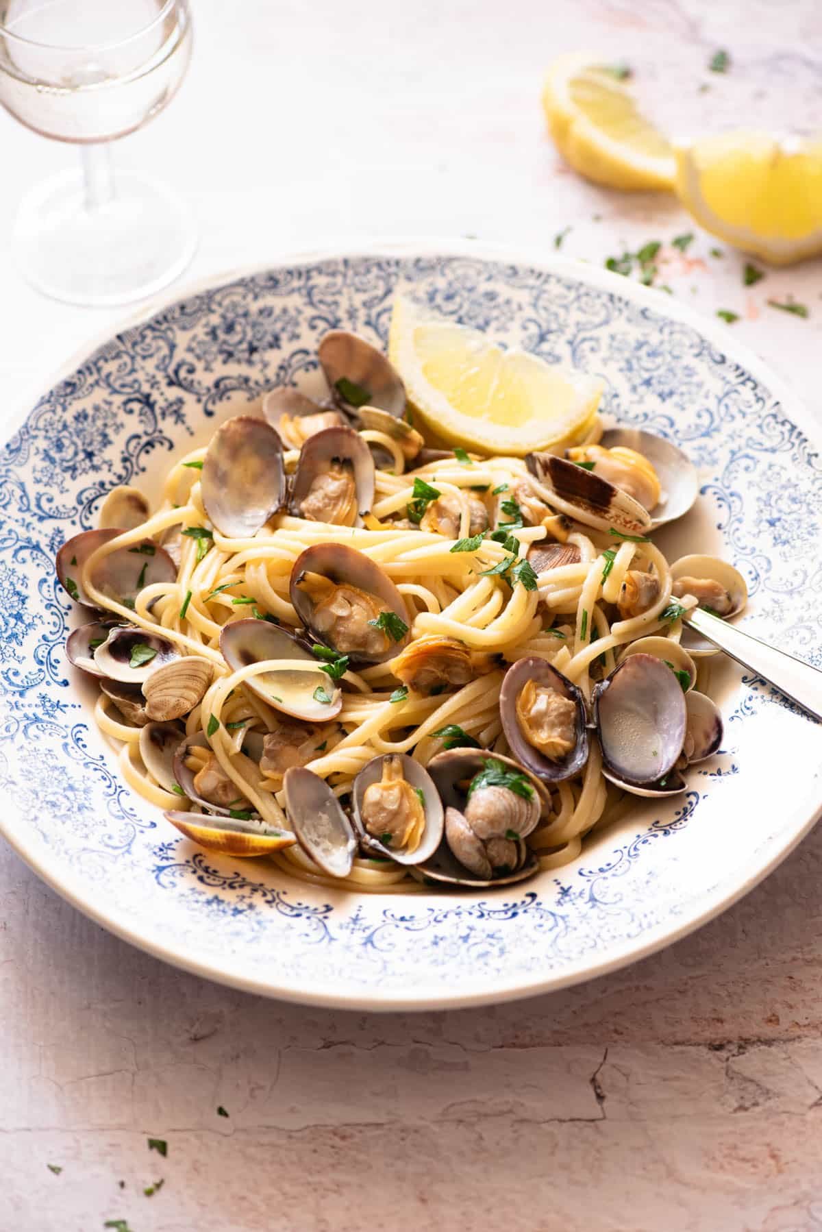 Linguine alle Vongole in a blue bowl with a slice of lemon at the side.