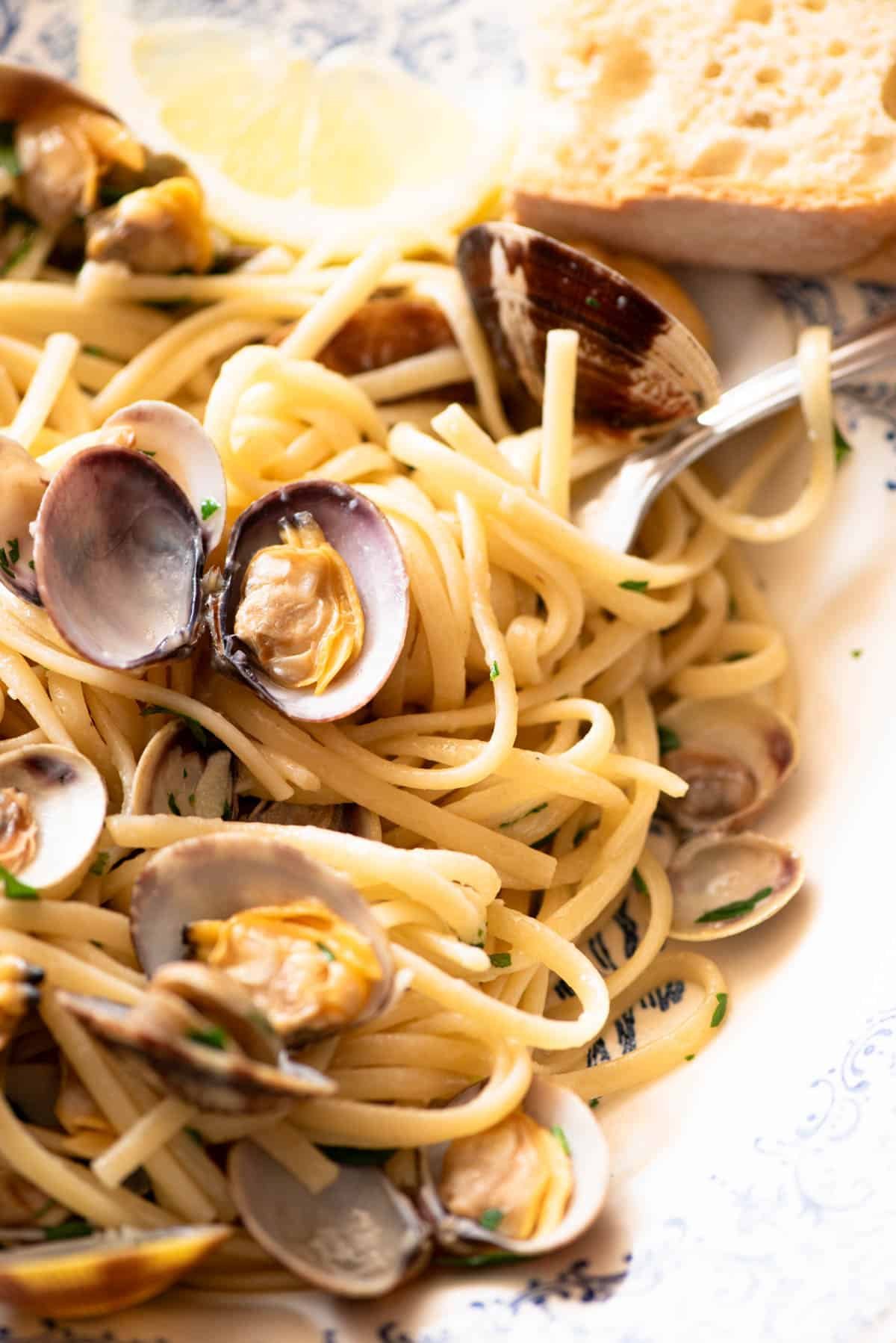 A close up of linguine pasta with clams, parsley and lemon in a bowl.