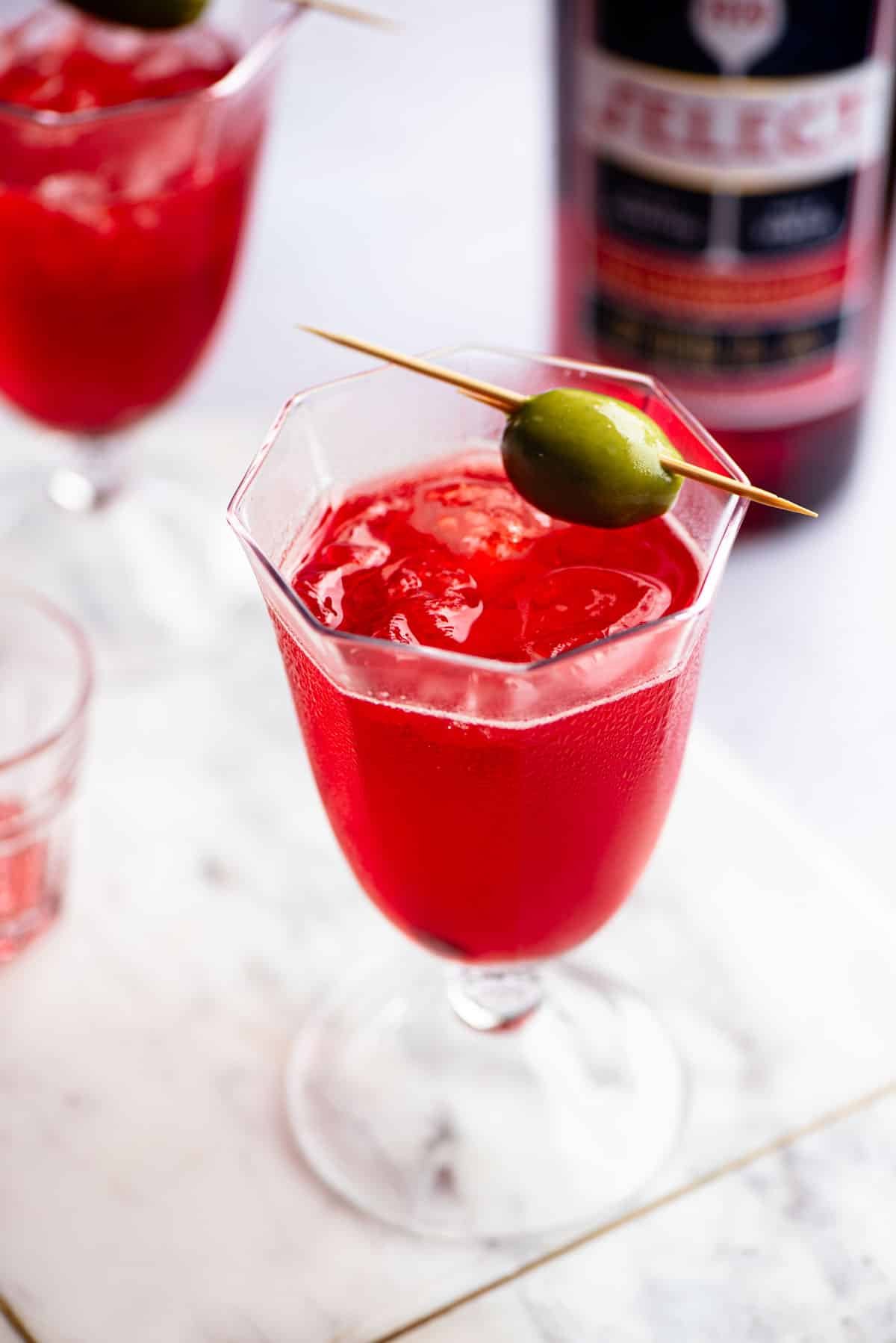 A close up of a Venetian Select Spritz on a marble chopping board topped with an olive.