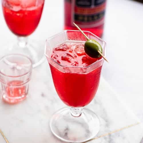 A select spritz in a glass topped with an olive.