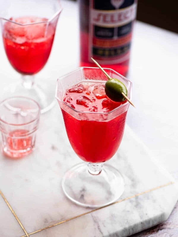 A select spritz in a glass topped with an olive.