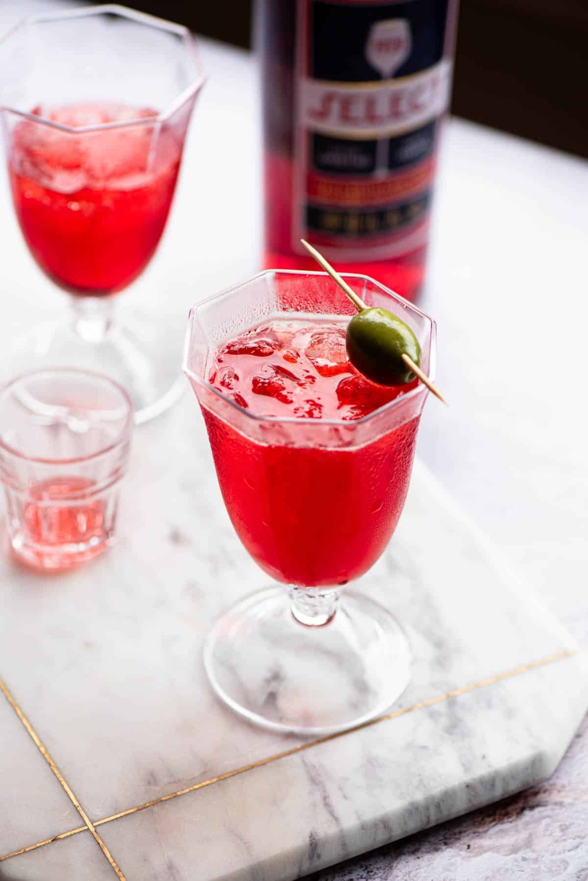 A select spritz in a glass topped with an olive.