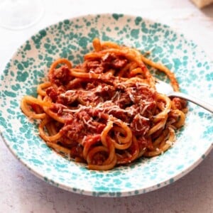 A cropped square image of Tuscan sausage pasta in a blue speckled bowl.