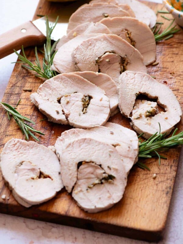 Slices of Italian roast pork on a wooden chopping board with a large knife and lemon at the side.