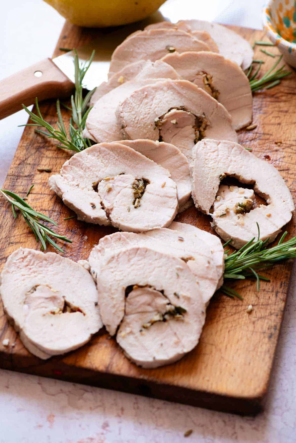 Slices of Italian roast pork on a wooden chopping board with a large knife and lemon at the side.